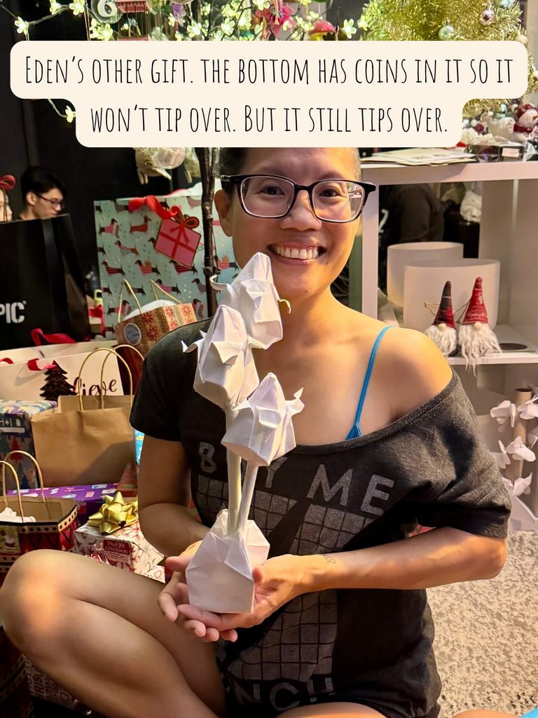 photo of me holding Eden's 2nd gift to me, a folded paper cup holding three folded and colored paper roses.
